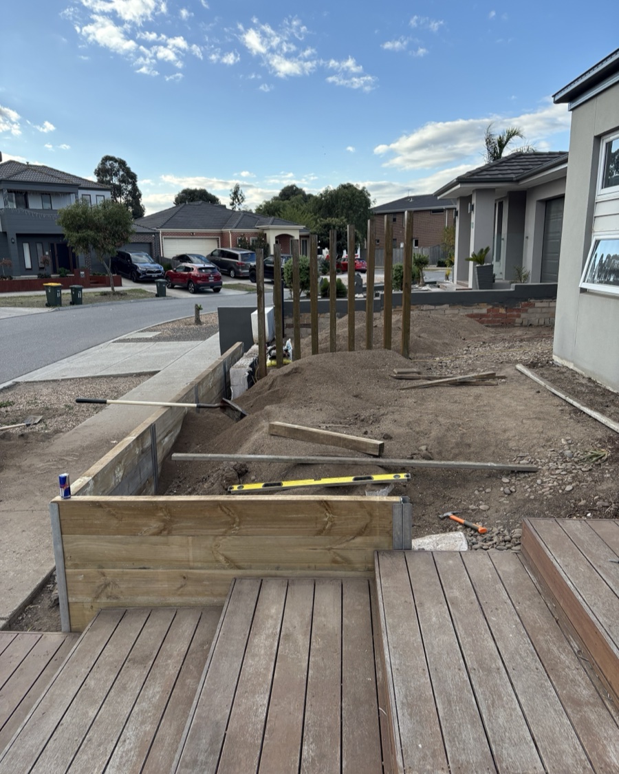 New-build front yard mid-construction, timber retaining wall framing on bare graded soil